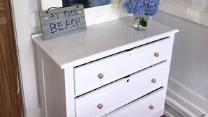 A white dresser with three drawers, a mirror above it, and a blue hydrangea vase on top. - Walk to the Beach! (Middletown)