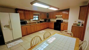 Una cocina con gabinetes de madera, un refrigerador, un microondas, una estufa y una mesa de comedor con sillas.