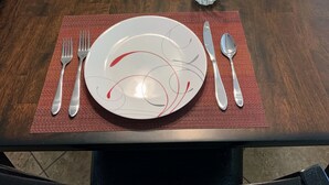 Una taula de dinar a punt, amb plats, coberts i gots, envoltada de cadires.