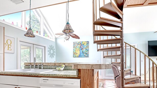 A modern kitchen with a built-in dishwasher, a wooden staircase, and a large window providing natural light. - Tropical Chalet w/ 3 King Bedrooms. 3 patios, and an Above-Ground Pool! (Sebastian)