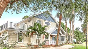 A two-story house with a balcony, surrounded by tropical plants and a well-maintained lawn.