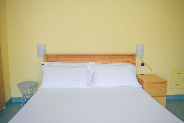 A bed with white linens, a wicker headboard, two wall-mounted speakers, a small round table, and a wooden nightstand with a drawer. - Prestige - Stella Marina - Apartment with terrace and sea view (Pineto)