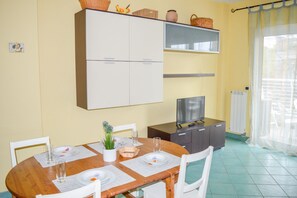 A dining area with a wooden table, white chairs, and a television on a cabinet. - Prestige - Stella Marina - Apartment with terrace and sea view (Pineto)