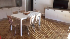 Een kleine keuken met witte kastjes, een eettafel met stoelen, een televisie en een vloer met een patroon.