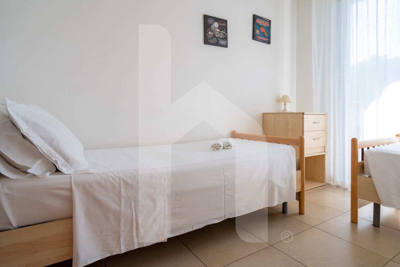 A single-bed room with a wooden headboard, a small wooden nightstand with a lamp, and two framed pictures on the wall.
