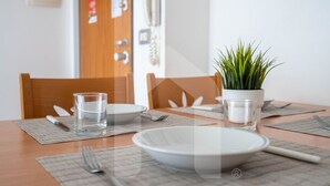 Une table à manger dressée avec des assiettes, des verres et des couverts, une plante en pot, et une porte sur laquelle sont fixés un téléphone et un détecteur d’incendie.
