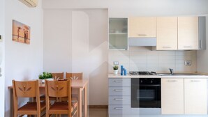 A modern kitchen with light-colored cabinets, a gas stove, and a built-in oven. There is a dining area with wooden chairs and a table, and a small potted plant on the table. - Holiday Rendez Vous 28 - Second floor apartment with side sea view (Pineto)