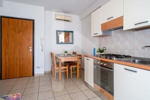 A compact kitchen with a stove, oven, and white cabinets. A dining table with chairs is positioned near the kitchen. - Holiday RendeZ Vous 39 - Third floor apartment with side sea view (Pineto)