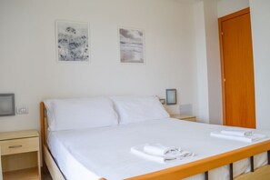 A neatly made bed with white linens and towels, a wooden headboard, and two framed artworks on the wall. - Holiday Rendez Vous 16 - First floor apartment with balcony and pool view (Pineto)