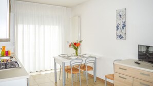 A compact room with a dining table set for four, a small kitchenette, a TV, and a radiator. - Holiday Rendez Vous 16 - First floor apartment with balcony and pool view (Pineto)