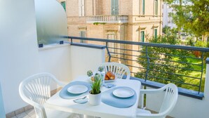 Ein Balkon mit Tisch für zwei Personen, weißen Stühlen, einem Blumentopf und einem Croissant.