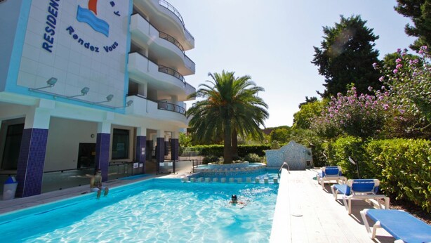 Ein Hotel mit Swimmingpool, Liegestühlen und Palmen.