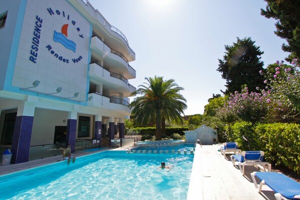 A hotel with a swimming pool, lounge chairs, and palm trees.