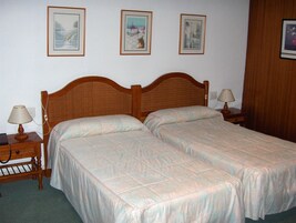 Una cama doble con cabecera de madera, dos mesitas de noche con lámparas, y tres cuadros enmarcados en la pared.