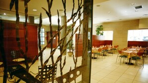 Un espace repas avec des tables et des chaises, une cloison en verre ornée de branches et une plante en pot.