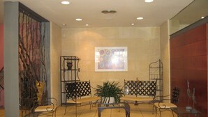 Un hall d’entrée avec un sol carrelé, des meubles en métal, une table basse au centre et un tableau abstrait aux couleurs vives accroché au mur.