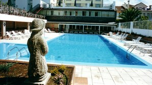 Une piscine avec des chaises longues et une statue en pierre.