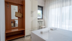 Een hotelkamer met een bed, een kledingkast, een spiegel, een raam met gordijnen en een klein tafeltje.