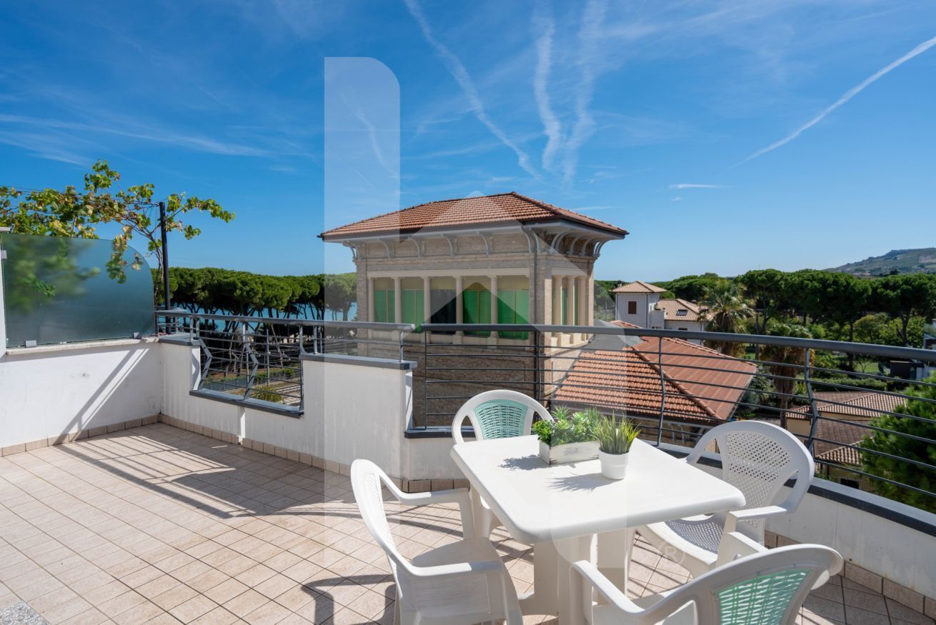 A rooftop terrace with a table and chairs, a view of a building with a red roof, and a clear blue sky.