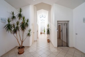 A hallway with potted plants, a tiled floor, and a door leading to another room.