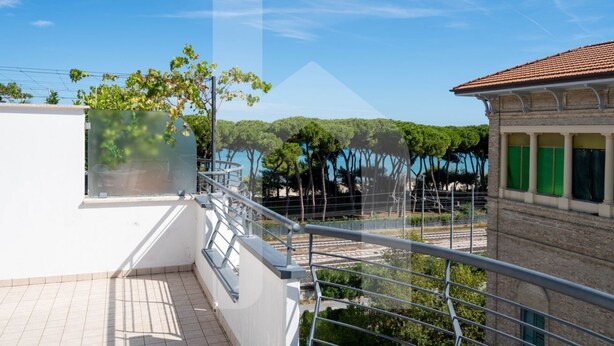 A balcony with a view of a forested area and a building with green shutters.