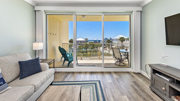 A hotel room with a balcony, a sofa, a TV, and a dining area with chairs and a table. - Beach Getaway in Peaceful Location! Pool~Hot Tub~Sun Deck~Gulf Views~King Beds (Gulf Shores)