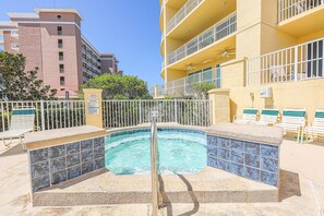 Une piscine dont le bord est revêtu de carrelage, entourée d’une clôture blanche et jouxtant un bâtiment doté de balcons.