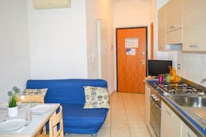 A compact kitchen with a stove, sink, and a blue sofa with cushions.