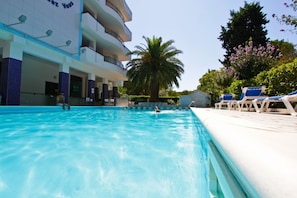 A swimming pool with a person swimming, a palm tree, and lounge chairs.