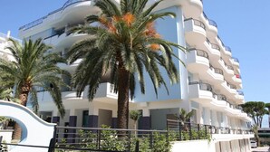 Hotel de diverses plantes amb balcons, palmeres i un cel blau clar.