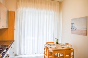 A dining area with a table set for four, a stove, and a window with sheer curtains.
