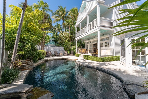 Relax in a serene outdoor space surrounded by lush vegetation and a well-maintained garden, with a large pool and modern architecture.