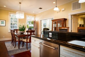 A kitchen with a wooden dining table, chairs, a chandelier, and a built-in refrigerator. - Key West Oasis - Truman Annex Estate (Key West)