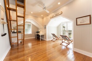 Relax in this spacious room with a high ceiling, featuring a wooden floor, ceiling fan, and a dining area with a table and chairs.