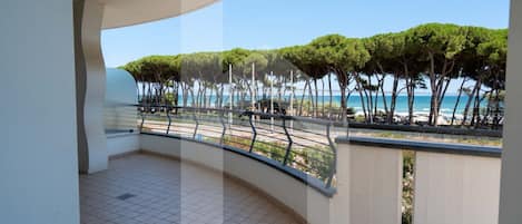 A balcony with a curved railing overlooking a beach with trees and the sea.