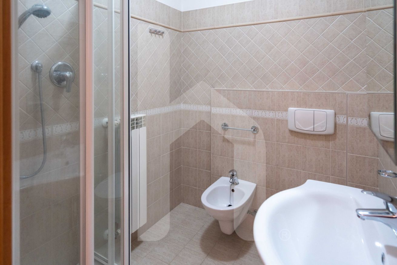 A bathroom with a glass-enclosed shower, a bidet, and a sink.