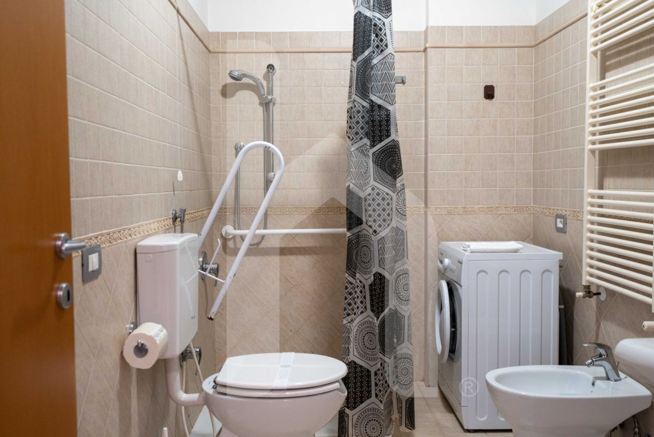 A compact bathroom with a toilet, sink, shower, and a washing machine.