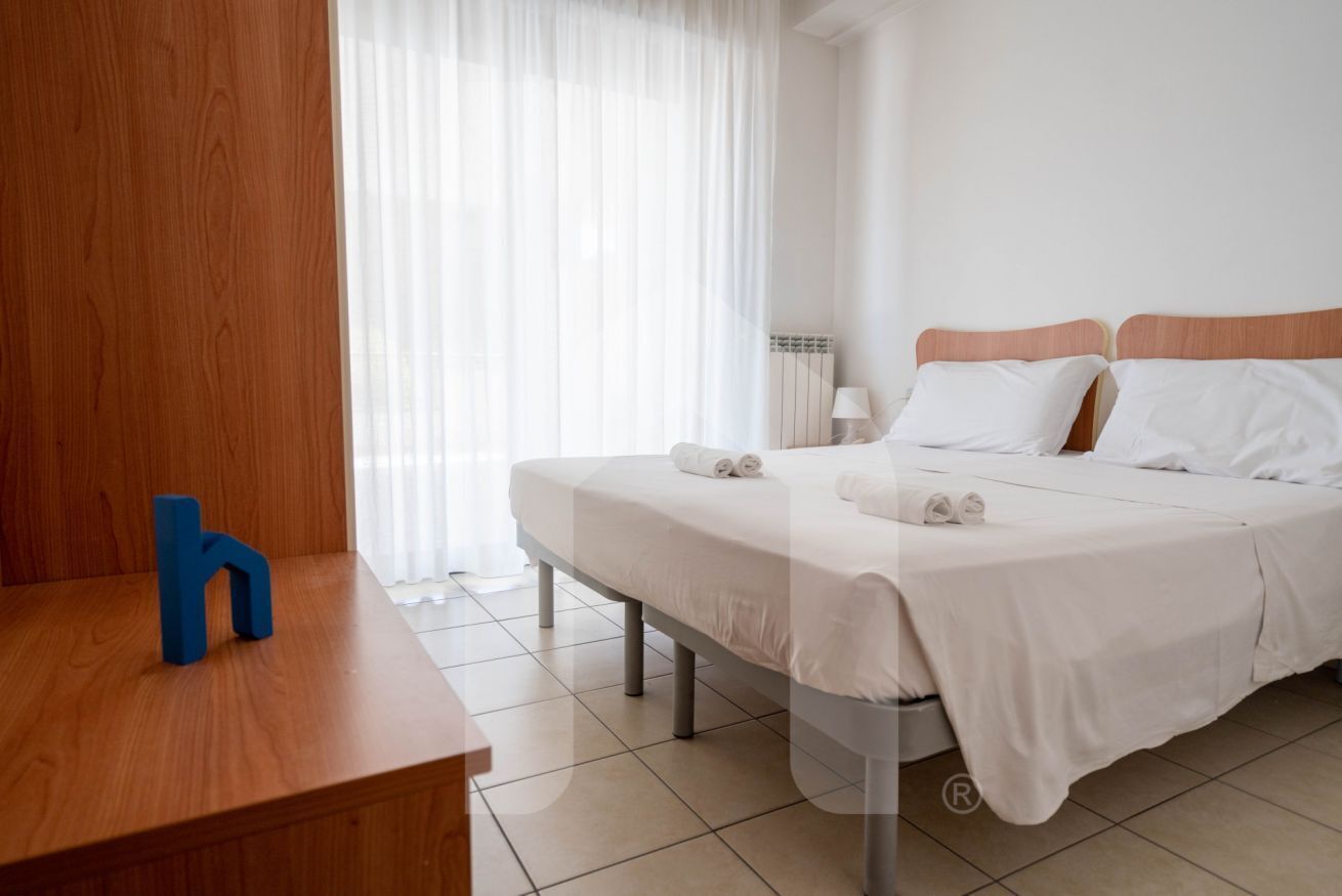 Una habitación de hotel con una cama, una mesita de noche, una lámpara y una letra 'h' de madera sobre la mesa.
