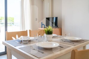 Une table à manger dressée avec des assiettes, des couverts et un verre, avec une plante sur la table et un téléviseur en arrière-plan.