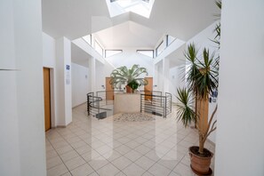Un vaste espace intérieur doté d’un haut plafond, d’un espace de détente circulaire central agrémenté d’une plante en pot et d’une grande fenêtre laissant entrer la lumière naturelle.