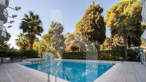 Piscina retangular com escada de metal, rodeada por um deck revestido de azulejos.