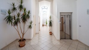 Um corredor com plantas em vasos, piso de azulejos e uma porta que dá para outro cômodo.