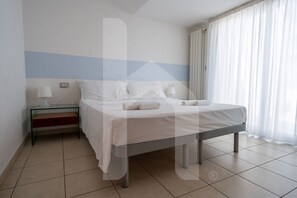 Ein Hotelzimmer mit Bett, Nachttisch, Lampe und einem Fenster mit Vorhängen.