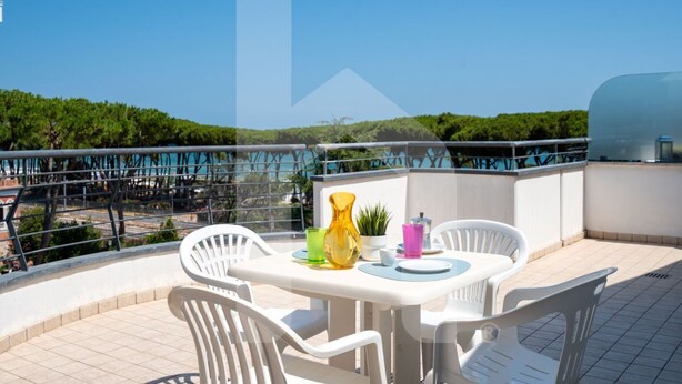 Terraço no telhado com mesa redonda e cadeiras brancas, um vaso de planta e bebidas coloridas.