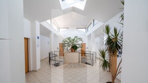 Um espaço interno amplo com teto alto, área de estar circular central com planta em vaso e uma grande janela que proporciona iluminação natural.