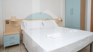 A hotel room with a bed, a nightstand, a lamp, a wardrobe, and a wall socket. - Résidence Holiday Rendez Vous is located in the heart of Pineto, just a few steps from the beach and the main street. Apartment 58, on the SABBIA floor, has a separate, west-facing entrance and a terrace with garden. (Foggetta)