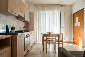 A compact kitchen with wooden cabinets, a stove, and a dining area with a table and chairs.