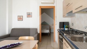 A compact living space with a kitchenette, a sofa, a dining table, and a TV. - Résidence Holiday Rendez Vous is located in the heart of Pineto, just a few steps from the beach and the main street. Apartment 58, on the SABBIA floor, has a separate, west-facing entrance and a terrace with garden. (Foggetta)