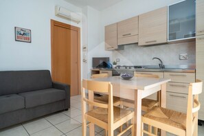 A compact kitchen with wooden cabinets, a dining table with chairs, a sofa, and a 'Please Do Not Disturb' sign.