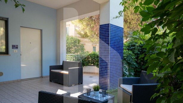 An outdoor patio with wicker furniture, a tiled column, and a door marked with the number 58. - Résidence Holiday Rendez Vous is located in the heart of Pineto, just a few steps from the beach and the main street. Apartment 58, on the SABBIA floor, has a separate, west-facing entrance and a terrace with garden. (Foggetta)